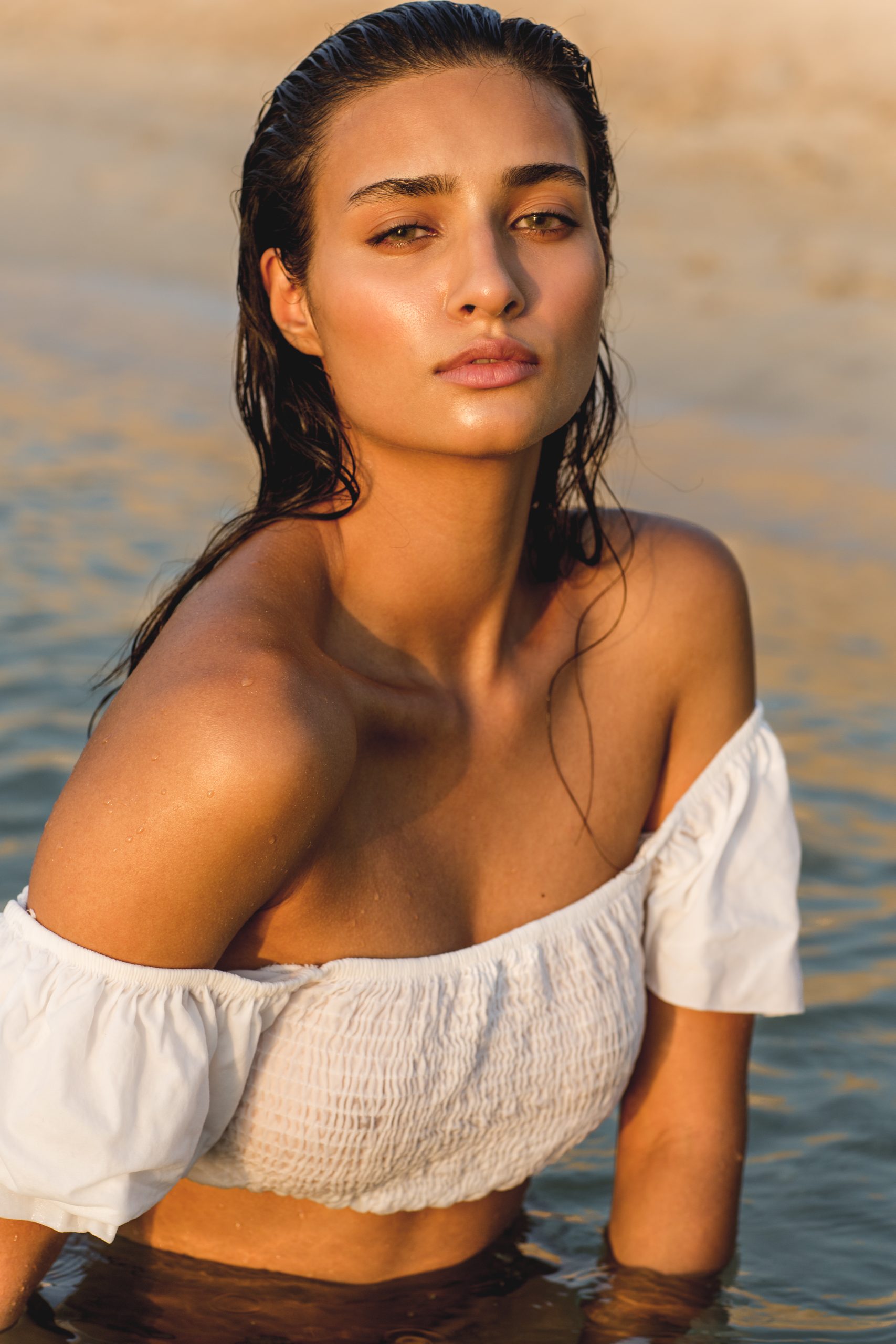 Portrait of beautiful sexy wet woman sitting inside the ocean water at the beach during golden hour.